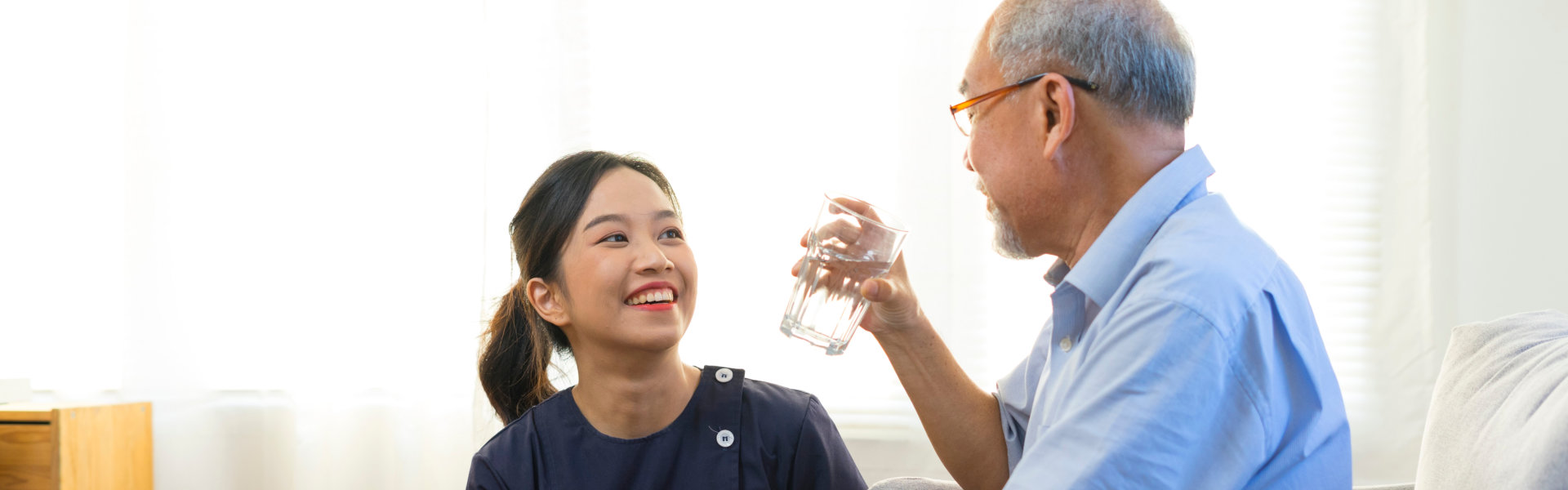 Smiling nurse giving glass of water to senior asian man in nursing home or assisted living facility.